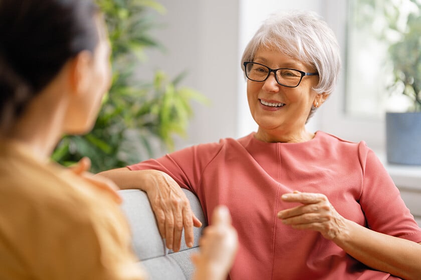 Beautiful mother and daughter are talking and smiling while sitting on couch at home.