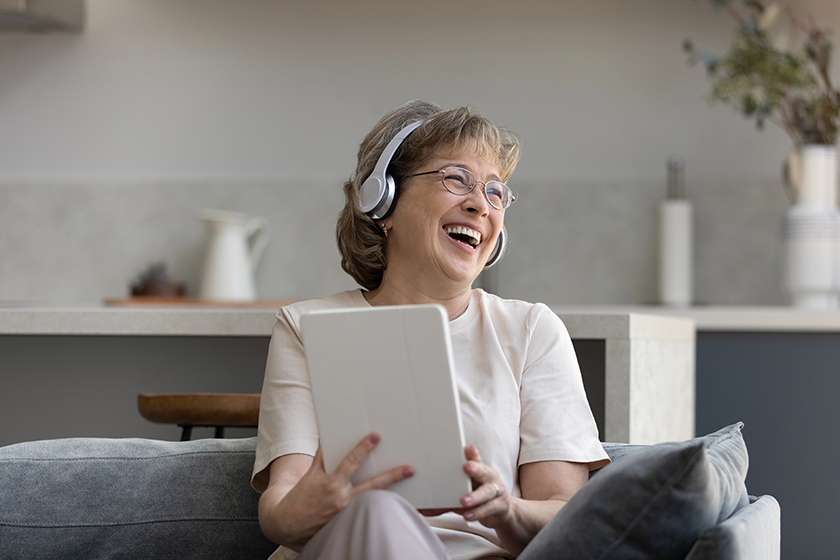 Happy elderly woman in headphones using digital touchpad gadget.