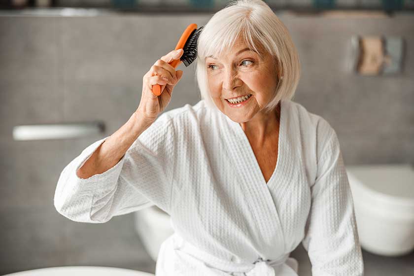 Lovely old woman brushing hair and smiling